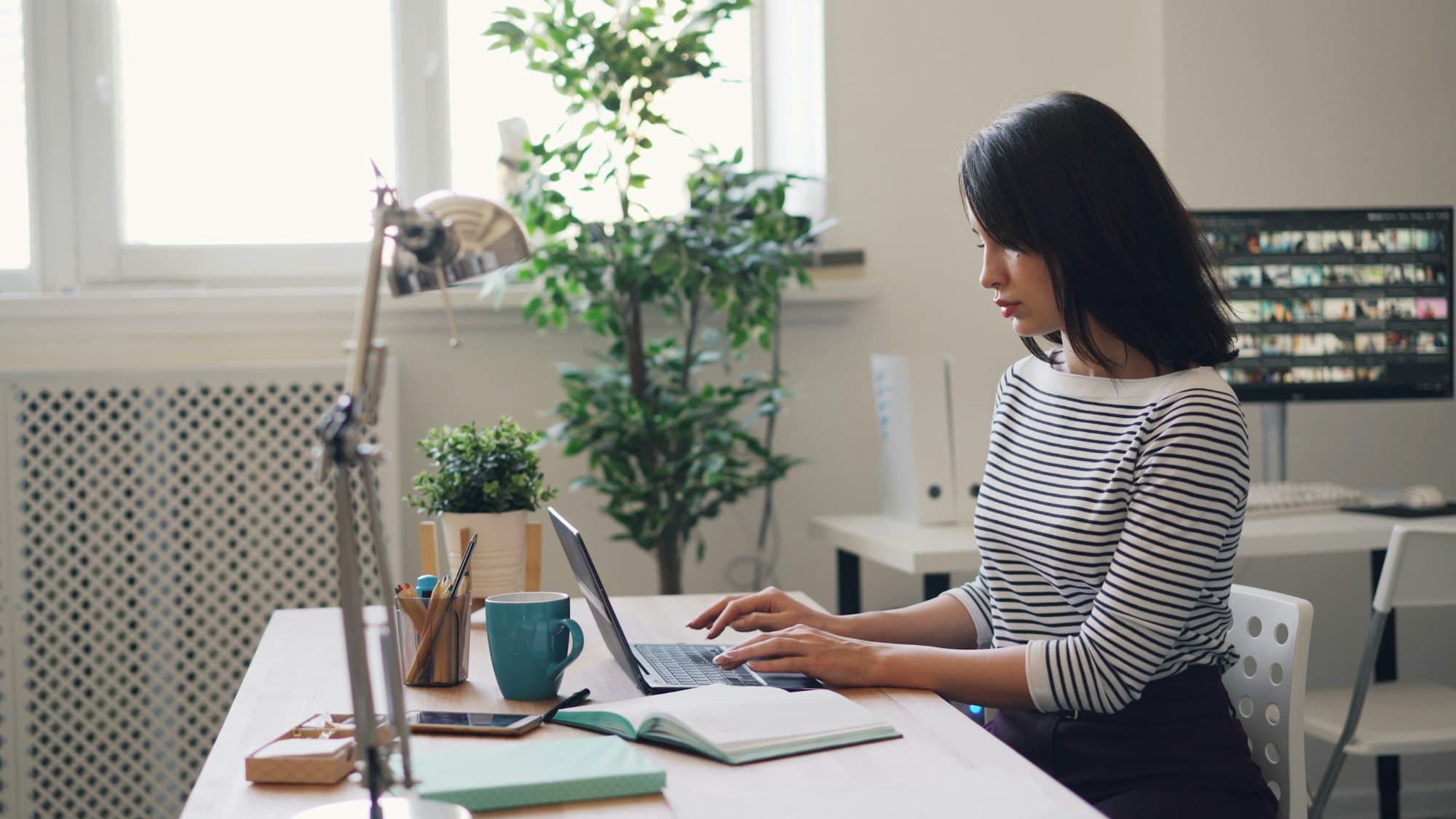 A professional working at a laptop by a bright window.