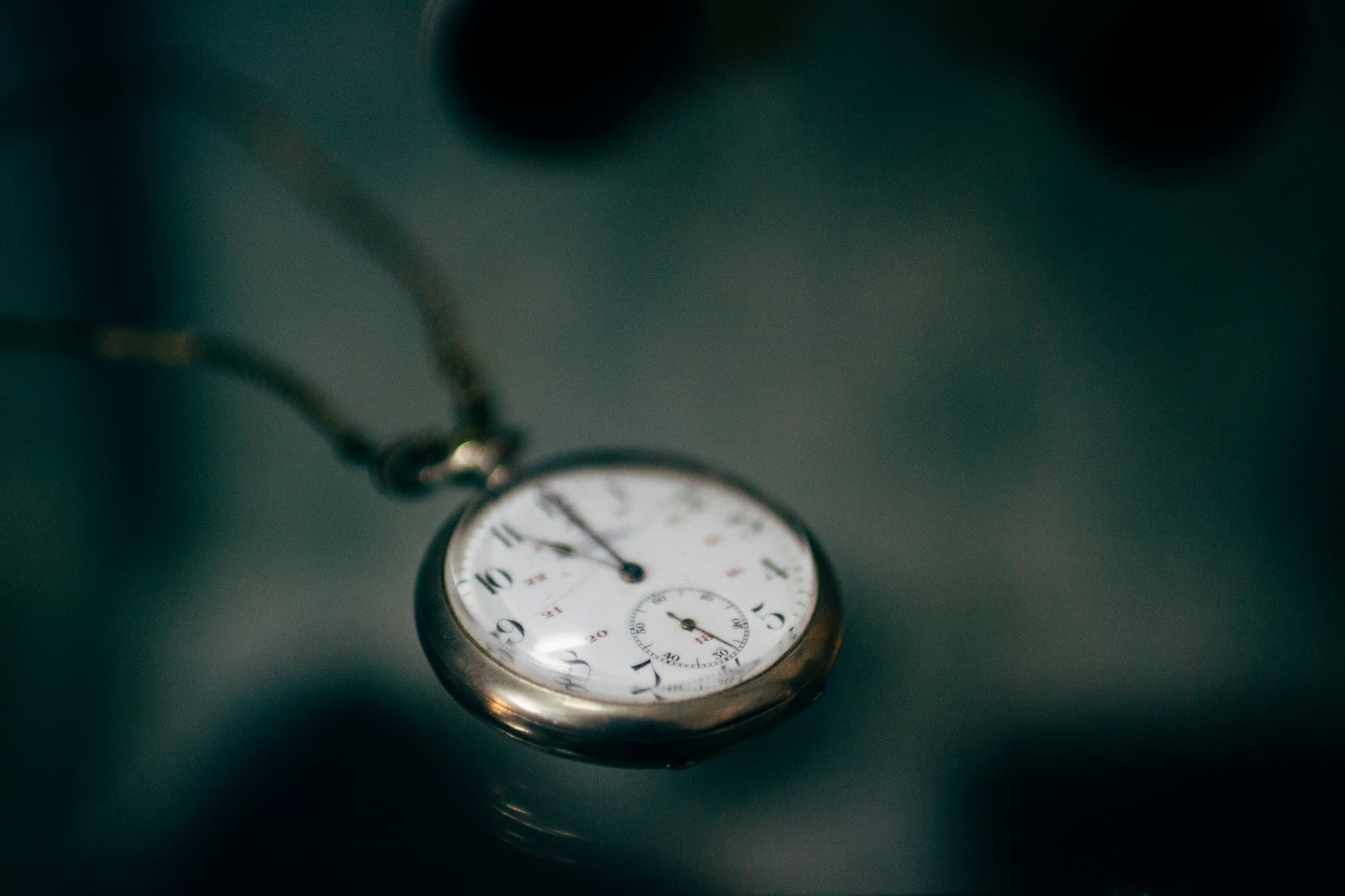 A pocket watch resting on a soft teal surface.