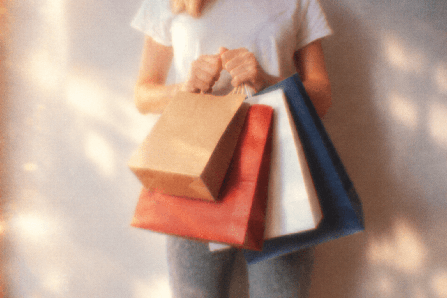 A shopper holding paper bags in soft sunlight.